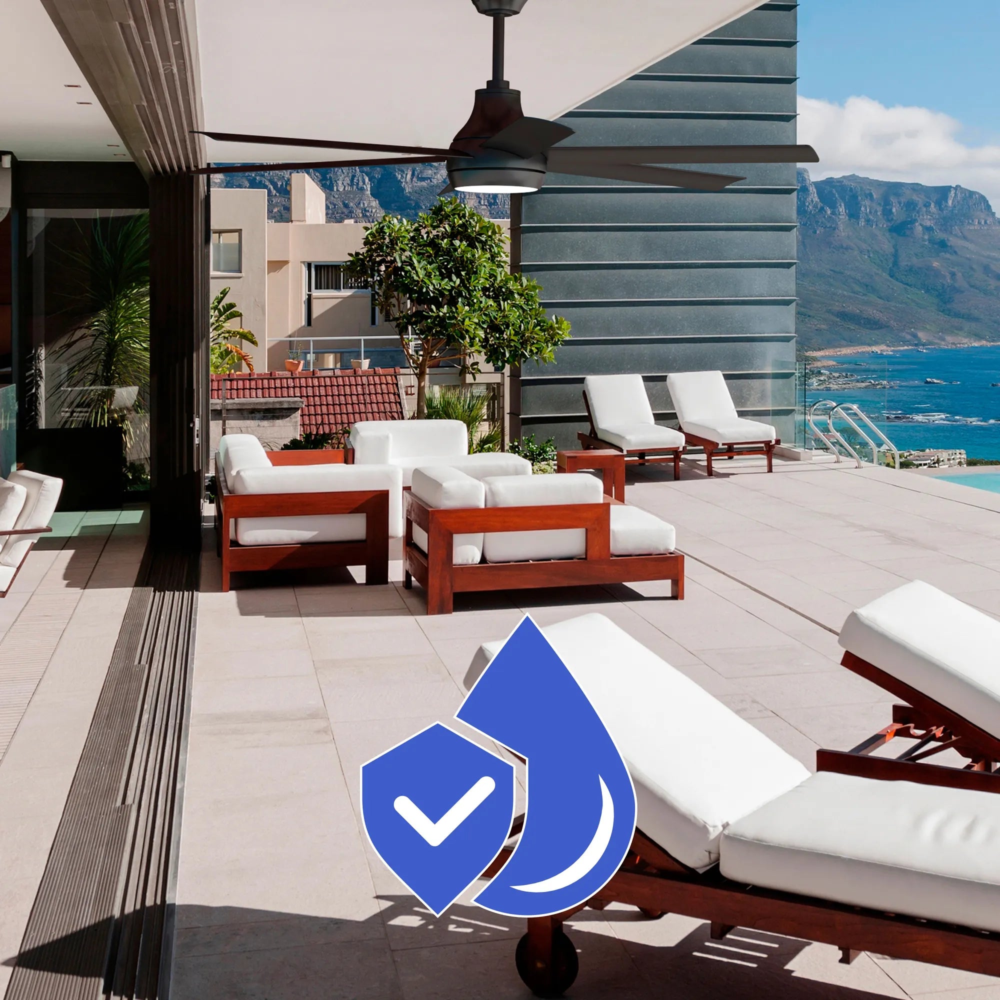 Bresio Ceiling Fan installed above a modern coastal patio with white cushioned wooden lounge chairs, showcasing corrosion-resistant construction with a blue water-and-shield icon.