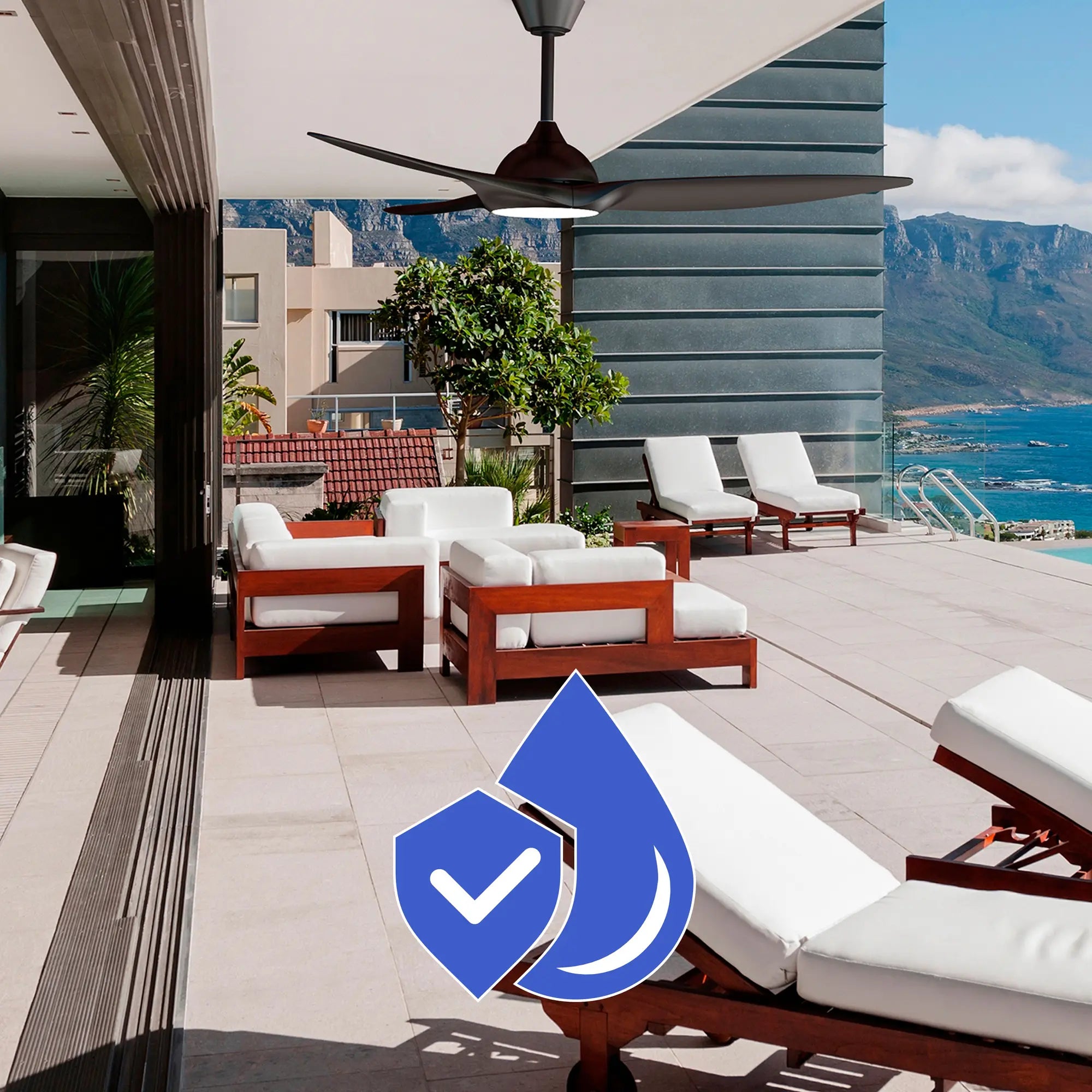 Slique Ceiling Fan installed above a modern coastal patio with white cushioned wooden lounge chairs, showcasing corrosion-resistant construction with a blue water-and-shield icon.